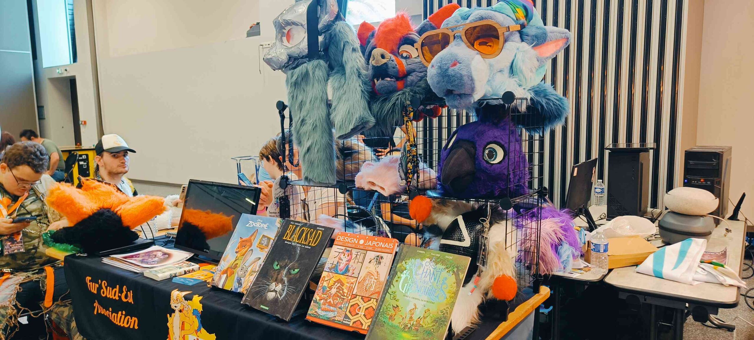 Le stand de Fur’Sud-Est avec des livres et des têtes de fursuit